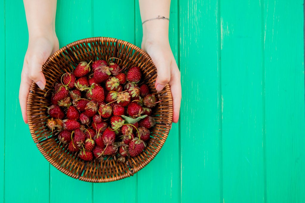 vue de dessus des mains de femme tenant un panier avec des fraises